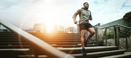 Fitness, city and black man running on steps outdoor, exercise and training healthy body in the morning at sunrise. Sports, cardio and African athlete on stairs for workout, wellness and lens flareの写真素材