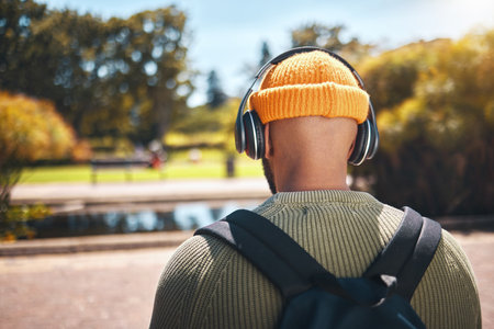 Back, music headphones and student outdoor, listening to audio or streaming sound online. Radio, podcast and man at park in nature, walking and hearing education media at university campus or collegeの写真素材