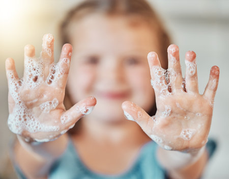 Soap, washing hands and kid with foam for cleaning, hygiene and wellness in bathroom at home. Health, child development and palms of young girl with water for protection for germs, virus and bacteriaの写真素材