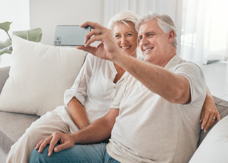 Happy, selfie and old couple on sofa in home, living room or apartment in retirement with post on social media. Mature, people and smile in profile picture, live stream or video call with smartphoneの写真素材