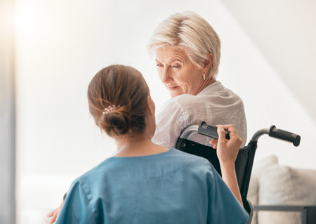 Old woman in wheelchair, help or caregiver talking for healthcare support at nursing home. Back, view or happy nurse speaking to senior patient or elderly person with a disability for empathy or hopeの写真素材