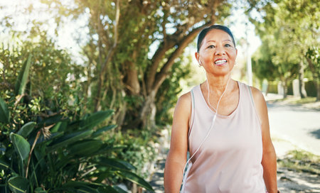 Fitness, music earphones and Asian woman outdoor for sports training, exercise and walking for healthy body. Happy, mature athlete listening to radio at park and streaming audio podcast to workoutの写真素材