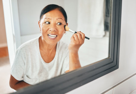Woman, mirror and brush makeup in home for foundation, cheek contour and grooming routine. Face, mature asian person and facial beauty powder for skincare, aesthetics or cosmetics tools in reflectionの写真素材