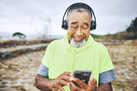 Phone, headphones and senior man hiking for health, wellness or cardio training on a mountain. Smile, cellphone and elderly male person scroll on the internet for music for outdoor trekking in woods.の写真素材