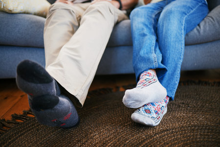 Legs, feet in socks and a couple on a sofa in the living room of their home together closeup to...