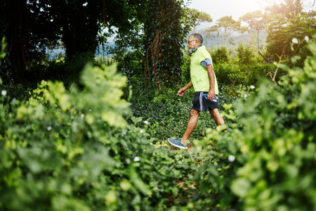 Senior man, fitness walk and forest in profile, green and outdoor for wellness in retirement. Mature person, exercise and workout for health, hiking and freedom in woods, countryside or nature parkの写真素材