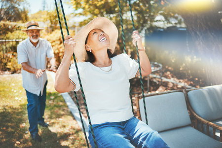 Woman, smile and fun on swing in retirement, playful and joy in summer vacation for quality time. Happy elderly people, support and love in relationship, funny and laugh for silly, goofy and holidayの写真素材