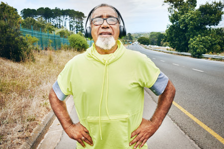 Outdoor, tired and senior man with fitness, headphones and fatigue with exercise, workout and sweating. Elderly person, runner or old guy with a headset, exhausted or breathing for wellness or healthの写真素材