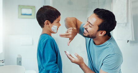 Shaving, bathroom and father teaching child about grooming, hygiene and facial routine. Happy, help and a young dad showing a boy kid cream or soap for hair removal together in a house in the morningの写真素材