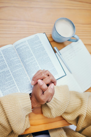 Bible, notes and hands of woman in prayer at desk in home, Christian faith or knowledge of God from...
