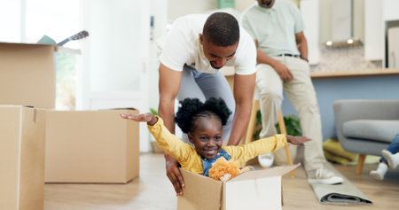 Father, child and playing in a box while moving house with a black family together in a living room. Man and a girl kid excited about fun game in their new home with a smile, happiness and adventureの写真素材