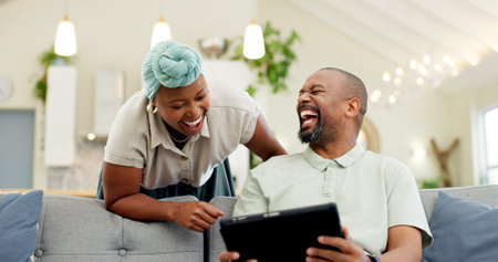 Black couple, laughing and tablet on a home sofa for streaming, meme and internet in a living room. African woman and man together to talk about tech, funny post or video on social media or networkの写真素材