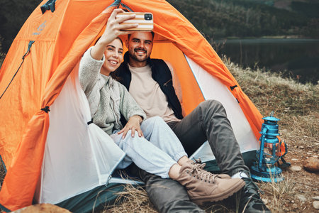 Couple, tent and camping selfie with smile, memory and holiday, web blog and morning in countryside. Man, woman and relax with vacation, social media post and adventure with love, outdoor and freedomの写真素材