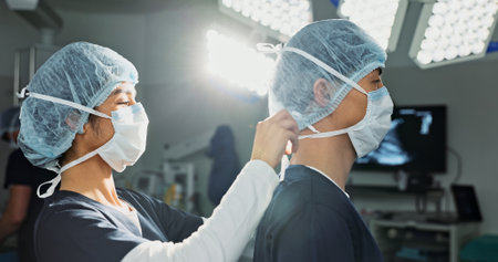 Surgery, hospital and doctors tie mask in operating room for medical service, preparation and operation. Healthcare team, safety scrubs and people with uniform for emergency, procedure and protectionの写真素材