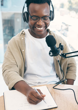 Live stream, podcast or black man with notebook, microphone or headphones with news broadcasting. Smile, African person or radio presenter with tech, public relations or writing with content creatorの写真素材