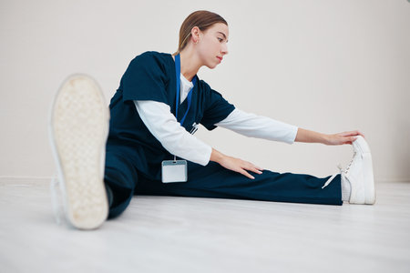 Hospital, medical and a nurse stretching on the floor of a studio, getting ready for healthcare or treatment. Legs, warm up and a confident young volunteer or medicine professional on mock upの写真素材