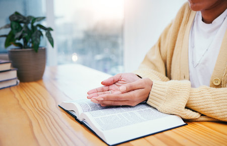 Bible, worship and open hands of woman in prayer, studying religion in home with Christian faith and knowledge of God. Reading, gospel and girl at table with holy book for spiritual praise and givingの写真素材
