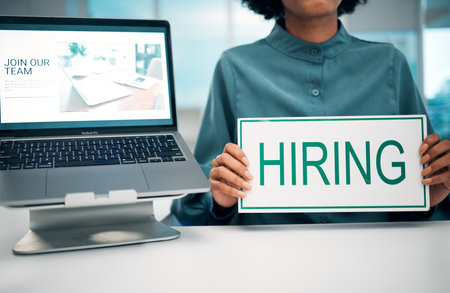Person with hiring sign, laptop and human resources with offer, recruitment and job opportunity at company. Onboarding, pc screen with website and HR hands to join team, poster and recruitingの写真素材