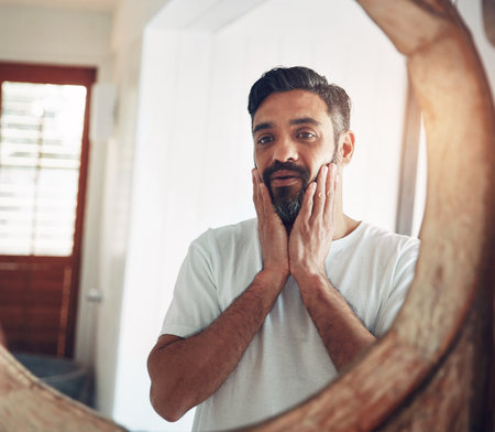 Mature man, mirror and reflection in home with thinking, wellness and beard for skincare, ideas and morning. Person, bathroom and check face for beauty, health and facial hair with routine in houseの写真素材