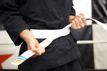 Man, hands and white belt in karate of martial arts beginner, training or discipline at dojo. Closeup of male person tying gi or ranking in self defense, arena or professional fighting sport matchの写真素材