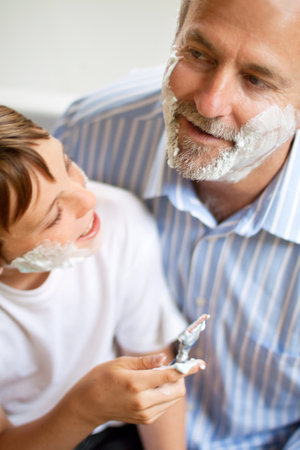 Family, father and son learning to shave in the bathroom of a home together closeup from above. Razor, shaving cream and a man teaching his boy child about skincare or grooming while bondingの写真素材