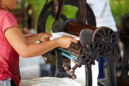 Rubber, farming and hands of person with roller in workshop, factory and agriculture warehouse. Manufacturing, production with worker machine for rolling latex, plastic and material plantationの写真素材