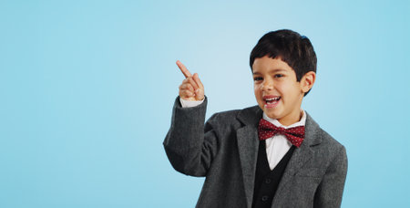 Pointing, face or happy child in studio for offer, discount deal or retail sale on mockup space or logo advertising. Business, funny or excited boy with smile, news or kids promo on blue backgroundの写真素材