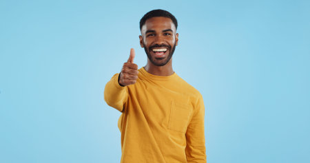 Face, smile and man with thumbs up in studio for support, motivation or vote on blue background....