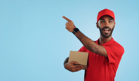 Advertising studio smile, delivery man and point at supply chain commercial, discount export info or distribution schedule. Courier service deal, mockup space and portrait person on blue backgroundの写真素材