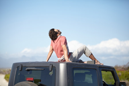 Travel, man and sitting on van roof for scenery, nature and fresh air on adventure or vacation in South Africa. Person, tourist or traveler on rooftop of car with sunglasses for view or road tripの写真素材