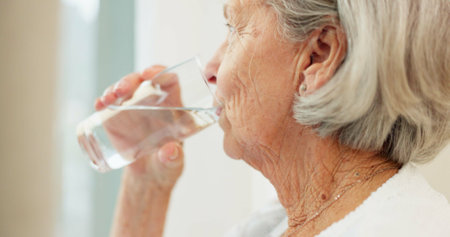 Healthy, hydration and senior woman drinking water for wellness and liquid diet detox at home. Thirsty, fresh and calm elderly female person enjoying glass of cold drink in modern retirement house.の写真素材
