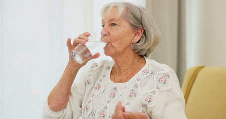 Water, pills and senior woman on a sofa with medicine for health, balance and aging wellness in her...