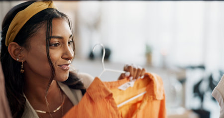 Sale, shopping and happy woman at a mall for clothes, outfit or thrift store fashion choice. Retail, decision or Indian customer check boutique fabric quality, clothing rack or discount deal searchの写真素材