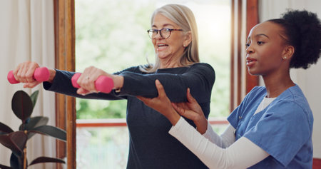 Physical therapy, exercise and senior woman with dumbbell, weightlifting and training arms and muscle. Strong, fitness and old person with nurse or physiotherapist to help in rehabilitation workoutの写真素材