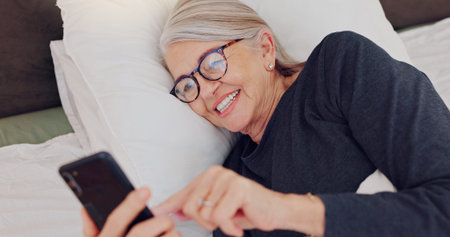 Happy, senior woman and reading with phone in bed or streaming funny, comedy or meme on social...