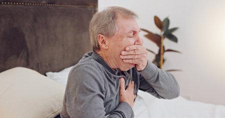Sick, cough and senior man in bed with allergies, flu or cold on a weekend morning at home. Illness, chest pain and elderly male person in retirement with asthma or infection in bedroom at house.の写真素材