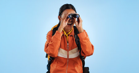 Hiking studio, binocular and woman watch trekking, backpacking and travel adventure view, sightseeing or bird watching. Wow, journey and happy camper vacation, freedom or discovery on blue backgroundの写真素材