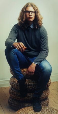 Man, portrait and fashion or style trendy clothes, wall background or long hair. Male person, model and face glasses for denim outfit or indoor confidence for edgy unique, serious cool or fresh lookの写真素材