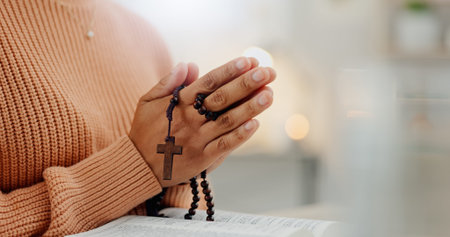 Closeup hands, rosary and a bible for prayer, spiritual support and hope from Jesus. House, God and...