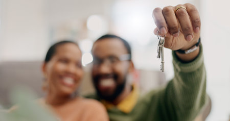 Hand, keys and couple with closeup in new home for fresh start, property or real estate investment with smile. African man, woman and happy for apartment, house and mortgage in blurred living roomの写真素材