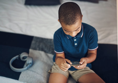 Youll find a variety of kids apps online. a young boy using a cellphone while sitting on his bed.