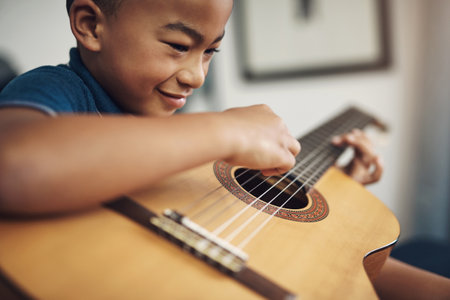 My friends love sports but I love playing the guitar. a young boy playing the guitar at home.の写真素材