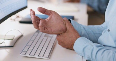 Businessman, hands and wrist in joint pain from injury, overworked or carpal tunnel syndrome at office. Closeup of man or employee with arthritis, ache or inflammation of palm on desk at workplaceの写真素材