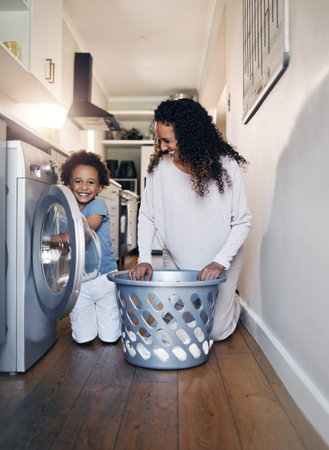 Adorable little African American boy with an afro smiling and faving fun while doing housework with...