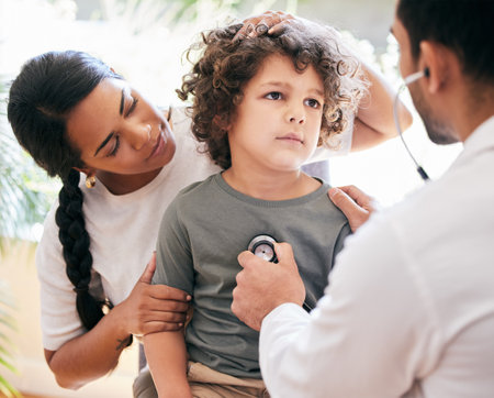 Please make him better. a little boy being examined by an unrecognizable doctor while his mother holds him.の写真素材