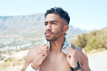 A young mixed race man looking serious standing topless in the road after exercising outside. Indian male focused and feeling satisfied with his daily workoutの写真素材