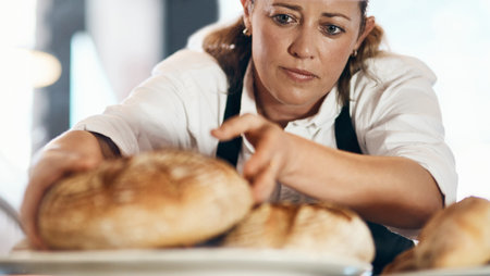 Freshly baked bread coming right up. a mature woman putting a selection of freshly baked breads on display in her bakery.の写真素材