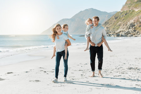 Today is all about the things we love doing as a family. a couple carrying their daughters on their backs while at the beach.の写真素材