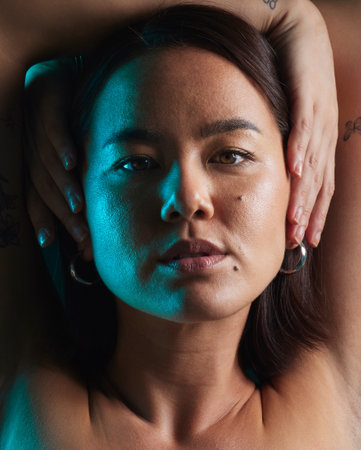 Neon, beauty and studio portrait of Asian woman with natural cosmetics, shadow or blue skincare light, glow or shine. Creative lighting, self love or face of person with makeup on dark backgroundの写真素材