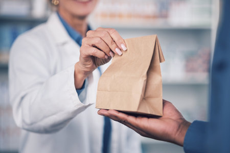 Woman, pharmacist and hands with medication for patient, healthcare or paper bag at the pharmacy. Closeup of female person or medical professional giving pills, drugs or pharmaceuticals to customerの写真素材